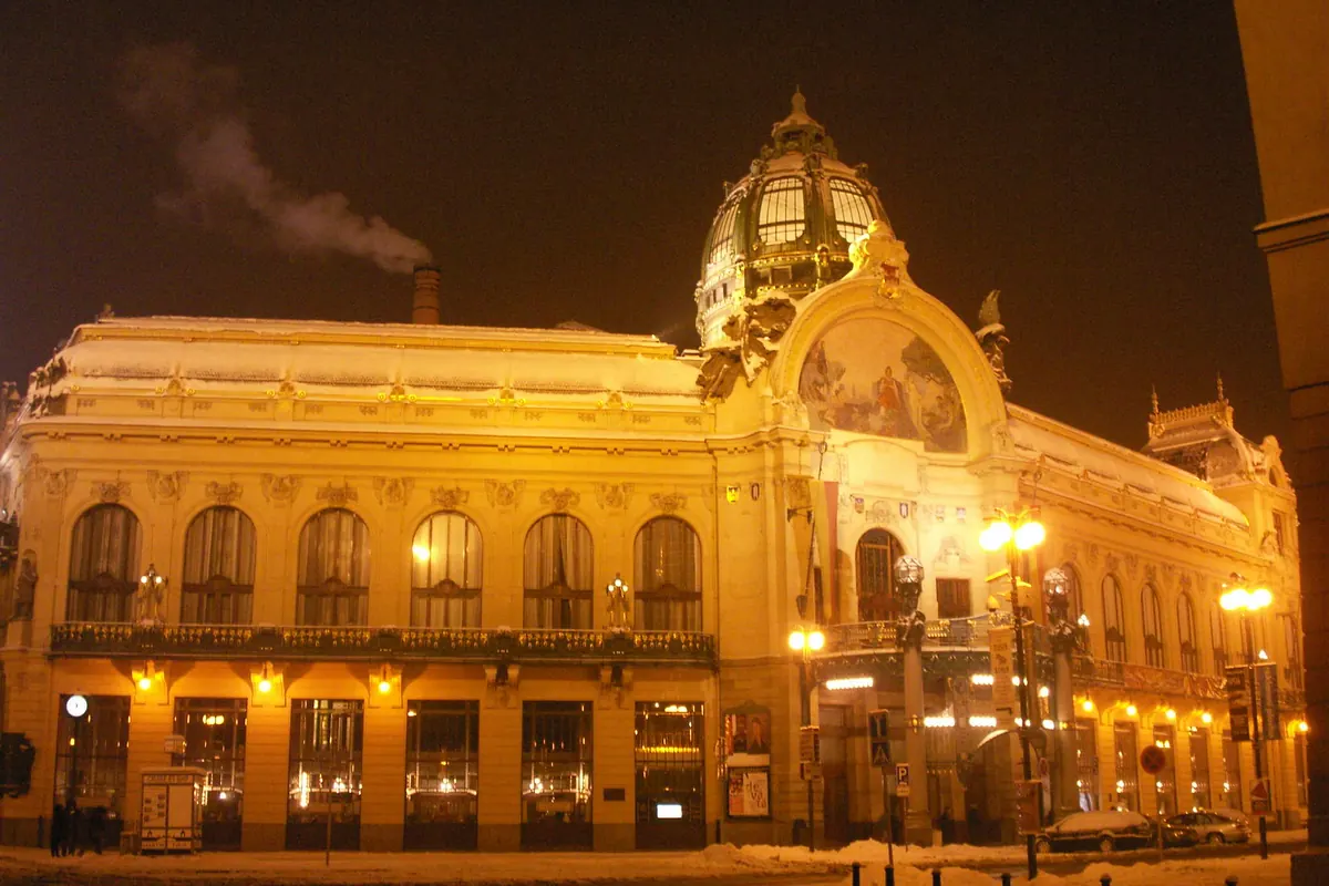 The Art Nouveau facade of the Municipal House in Prague lit with golden light at night, with a green dome.